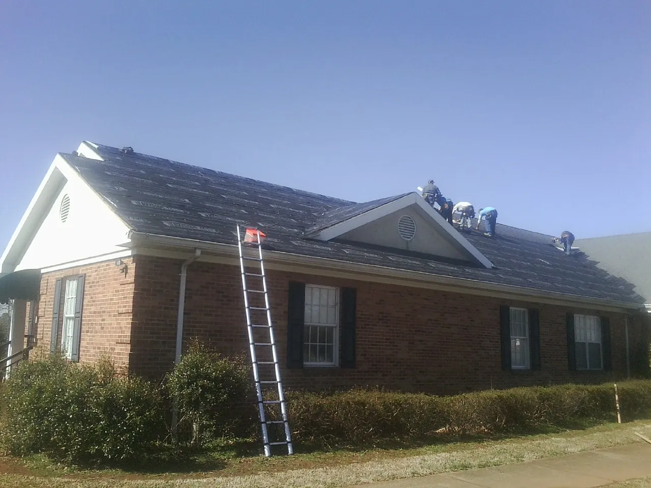 Crew tearing shingles off a brick ranch roof with a ladder set — Emergency Roof Repair work by our crew in Fulton